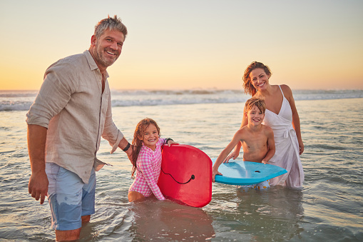 Family, beach and body board, kids with parents in water on summer holiday. Mom, dad and children surfing in ocean at sunset in Australia. Freedom, fun and vacation, happy man and woman play in waves