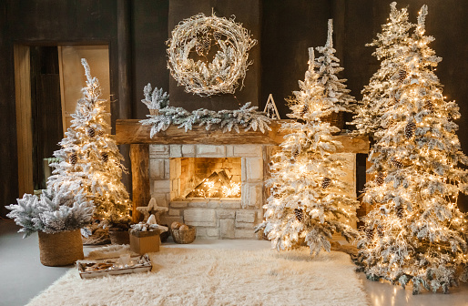 The interior of a room with a fireplace, Christmas trees with artificial snow and garlands, a blanket and a tray with hot drinks. The magical atmosphere of Christmas