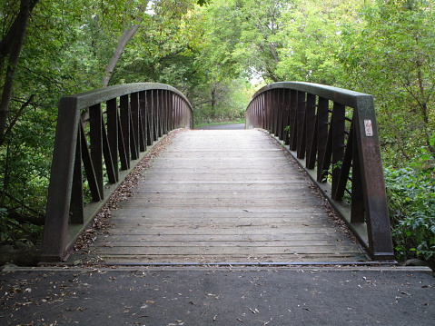 curved wooden bridge with iron railings leads to unknown place