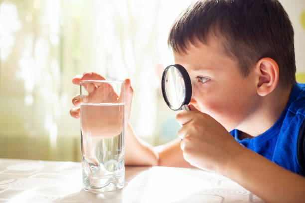 虫眼鏡越しにコップの中の水を見つめる少年少年 - magnifying glass lens holding europe ストックフォトと画像