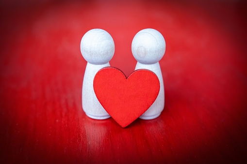 two wooden figures holding a red heart on red background