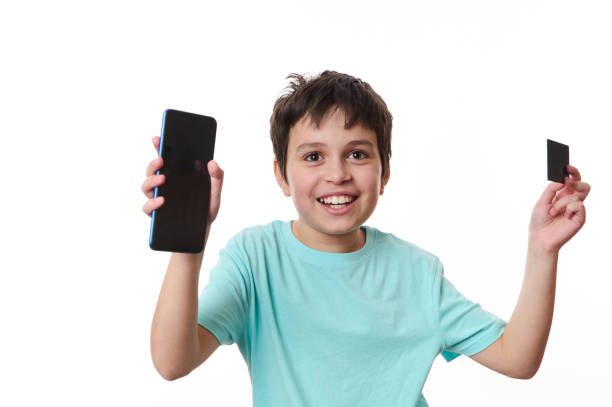 happy preteen boy holding smartphone and atm card with advertising space for promo text, isolated on white background - paying children only retail childhood imagens e fotografias de stock