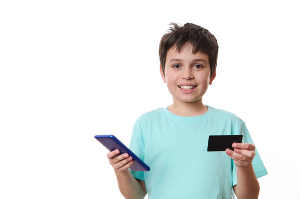 charming preteen boy, school child in blue t-shirt with smartphone and plastic credit card, isolated on white background - paying children only retail childhood imagens e fotografias de stock