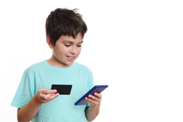 smart teenage boy transfers data from credit card to mobile app on smartphone, makes online payment, isolated on white - paying children only retail childhood imagens e fotografias de stock