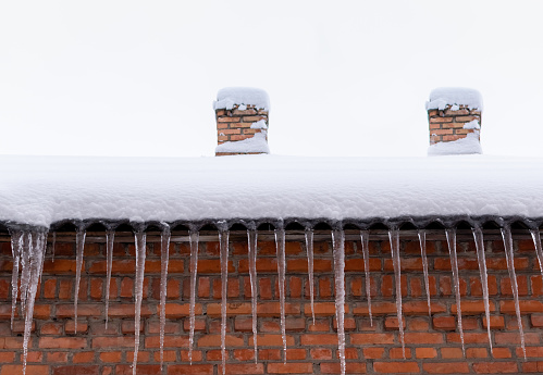Snow-covered roof of a house with chimneys and icicles against red brick wall