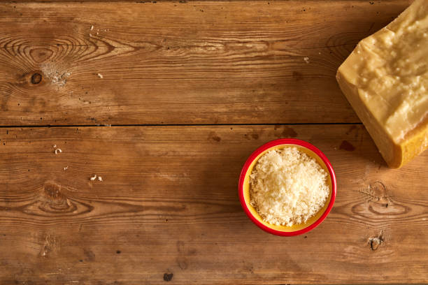 Overhead view of finely grated cheese in a bowl with block on wooden table