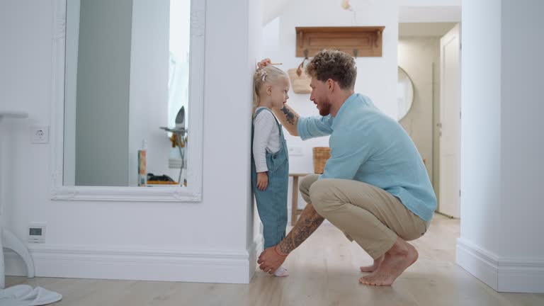 Cute blond father measuring her daughter's height at home