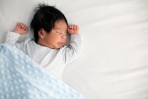 Cute baby in white bodysuit sleeping, adorable newborn child infant with closed eyes lying on back on comfortable bed white sheet, relaxing resting alone, fall asleep, childhood concept