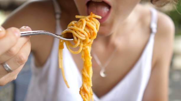 close-up of a young blonde woman with a nose piercing eating pasta with balonez sauce with great appetite. she wraps the pasta around the fork with precise, swirling motions. - gourmet enjoyment food freshness imagens e fotografias de stock