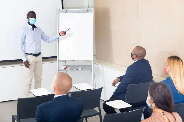 Man in protective mask giving presentation to colleagues at international business meeting