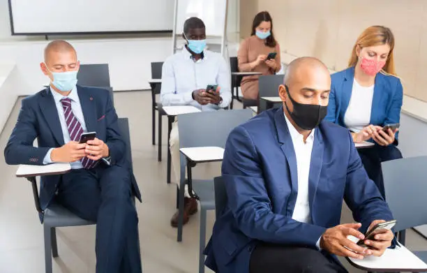 Group of business people in protective masks use smartphones at a business seminar