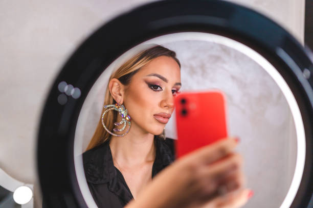 Beautiful young female make-up artist taking selfies in front of a ring light. She is showing off her make-up.