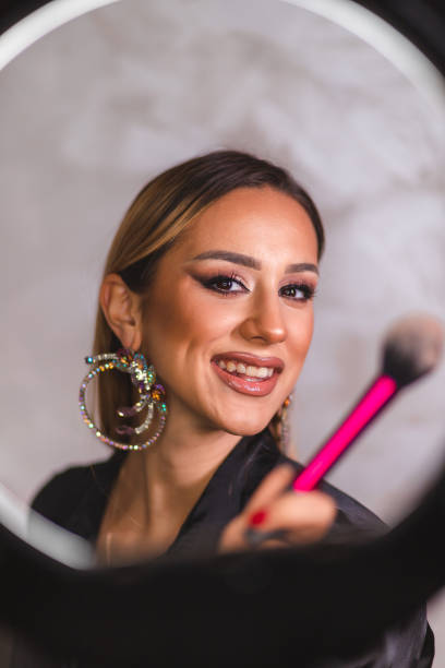 istock Beautiful young make-up artist posing with a make-up brush in front of a ring light 1444290363