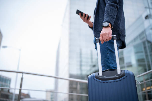 Businessman on a work trip using smart phone. Unrecognizable businessman with luggage and smart phone on a work trip. business travel stock pictures, royalty-free photos & images