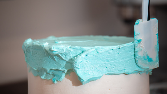 cake designer smoothing a frosted blank cake with turquoise light blue buttercream with spatula