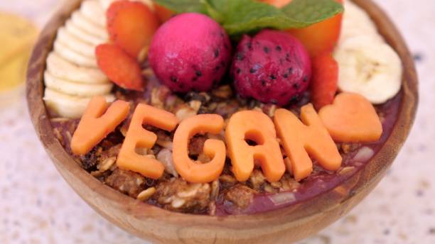 Plant-based breakfast concept. Dragon fruit smoothie with nuts, bananas, strawberries, served in a wooden bowl with large Vegan letters as decoration. Plant-based breakfast concept. Dragon fruit smoothie with nuts, bananas, strawberries, served in a wooden bowl with large Vegan letters as decoration. image based social media photos stock pictures, royalty-free photos & images