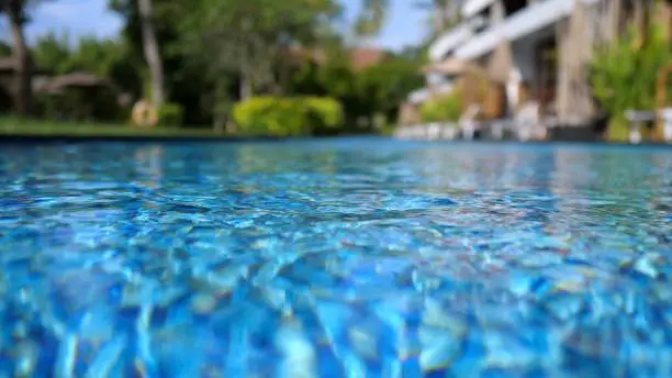 Photo of View from the pool above the water level. Clear water of pure blue color. In the background, a blurry view of a two-story villa. The concept of tropical villas for relaxation.