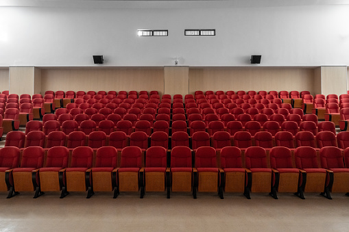 Single mature male person sitting in an auditorium. The rows of the chairs form a cross shape. Great symbol for christianity and loneliness.
