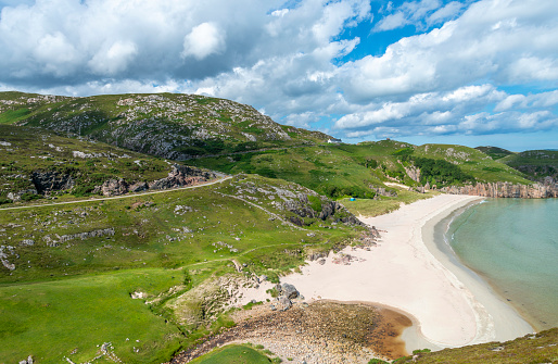 Scottish camping spot,stunning sands,calm Atlantic azure sea,sunny summertime morning,grass covered,underneath Beinn Ceannabeinne mountain,beautiful sand,steep grassy slope gives access to beach.