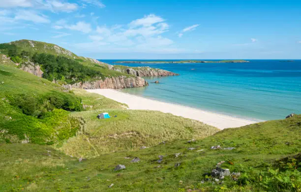 Scottish camping spot,stunning sands,calm Atlantic azure sea,sunny summertime morning,grass covered,underneath Beinn Ceannabeinne mountain,beautiful sand,steep grassy slope gives access to beach.