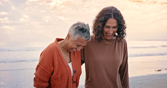 Elderly mother, beach and daughter with smile together on vacation, holiday or adventure by ocean. Senior woman, sea and conversation on happy walk on sand to laugh, relax or bonding with hug outdoor