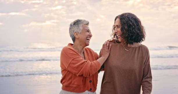 Happiness, friends and senior women at the beach enjoying nature, summer and outdoors together. Love, friendship and elderly best friends laughing, smiling and bonding by ocean on retirement holiday stock photo