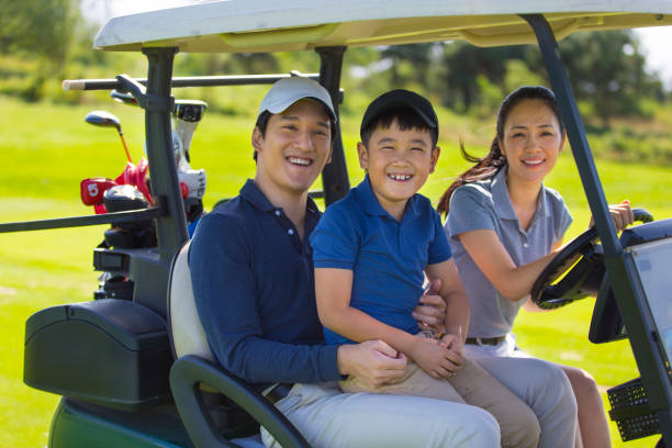 young east asian family of three driving a golf cart on a golf course in clear daylight - stock photo - golf course golf people sitting imagens e fotografias de stock