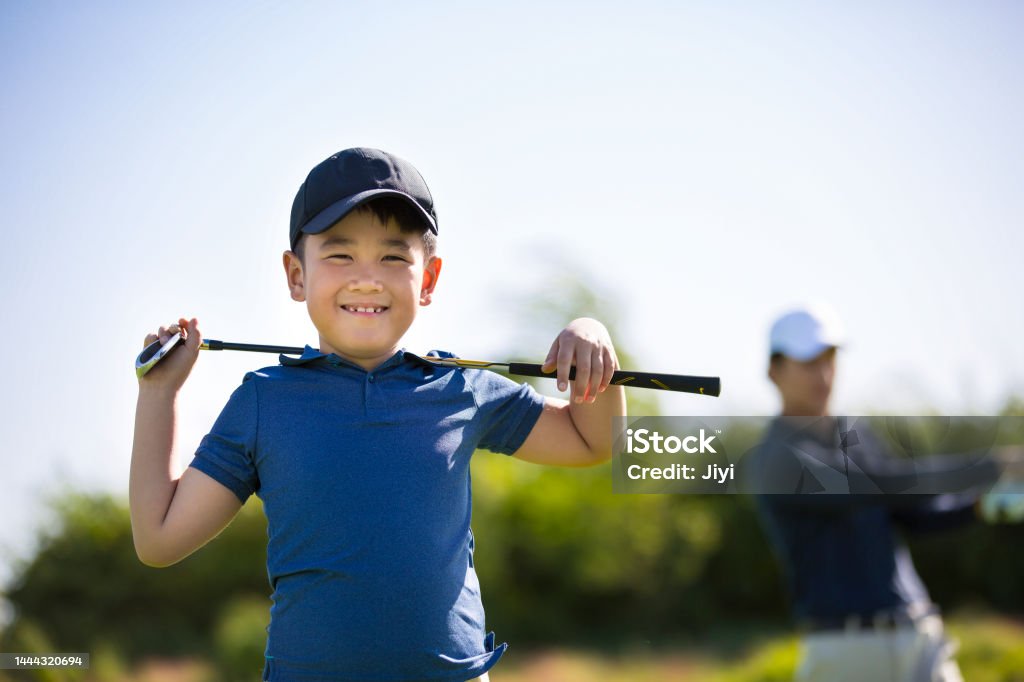 Young East Asian boy practicing golf on a sunny daytime golf course, carrying a golf club on shoulders - stock photo Suitable for golf, golf coach, sports, family, parent-child, noble sports, hobby cultivation, business and leisure, weekend activities, holidays, vacation, rich people's life, high consumption print advertising. Child Stock Photo