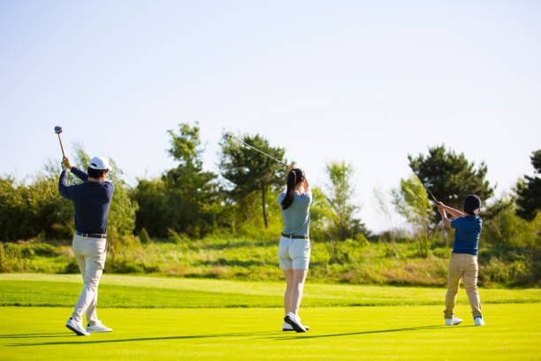 uma jovem família do leste asiático de três pessoas praticando seus tee shots em um campo de golfe ensolarado - stock photo - golf women female concentration - fotografias e filmes do acervo