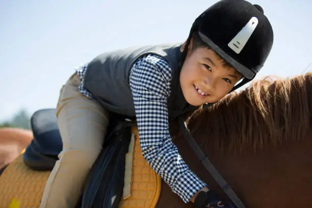 Photo of An East Asian boy practicing horsemanship and horseback riding in a horse farm under a clear sky - stock photo