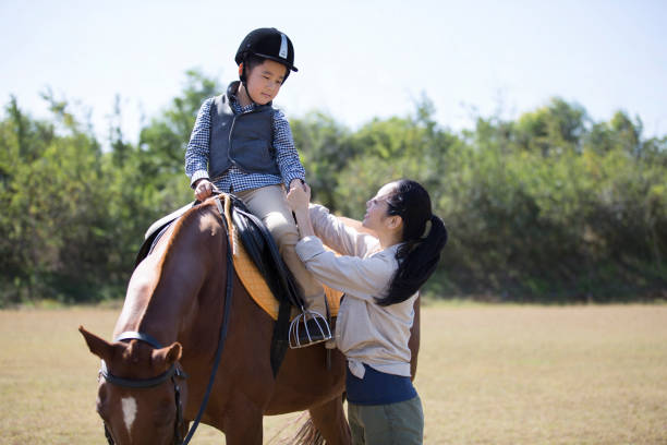 istock Mother and son practicing horseback riding on a meadow under a clear autumn sky, the boy on horseback, the mother lovingly teaching - stock photo 1444322228
