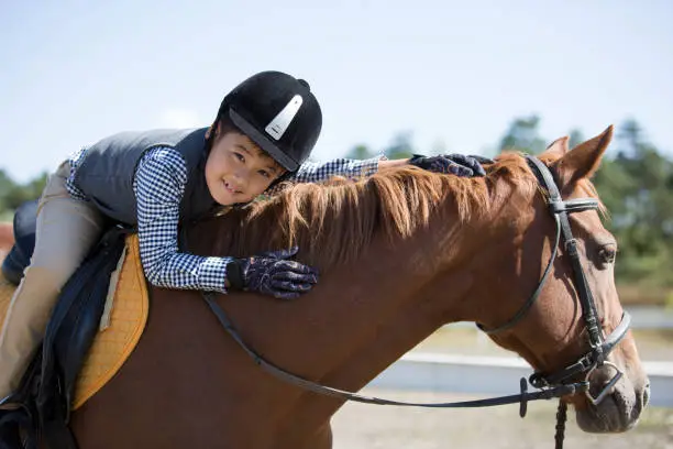 Photo of An East Asian boy practicing horsemanship and horseback riding in a horse farm under a clear sky - stock photo