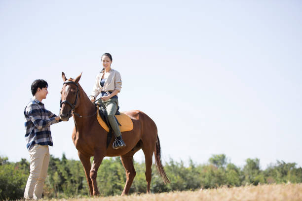 istock Young couple in a meadow under a clear autumn sky, the lady practicing riding, the man leading the horse - stock photo 1444322425