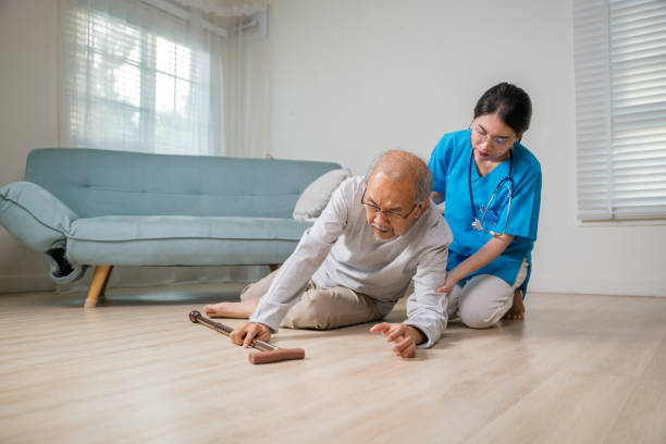 Paziente anziano anziano disabile con bastone da passeggio cadere sul pavimento e giovane assistente premuroso - foto stock