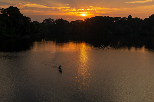 Man silhouette in canoe at sunrise, Amazon rainforest. Amazon river basin in Brazil, Peru, Ecuador, Bolivia, Guyana, Venezuela, Colombia, Suriname.