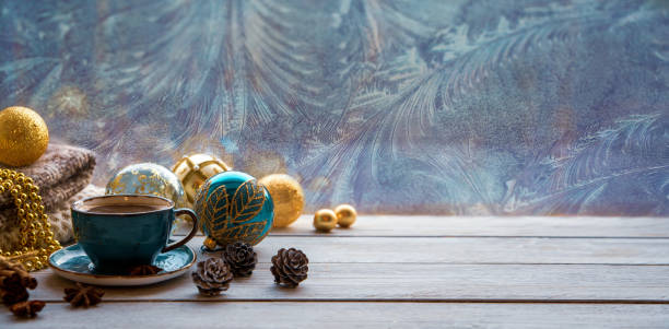 christmas mood, holiday atmosphere. a cup of coffee, christmas tree golden and turquoise balls, cones, star anise, cinnamon on a wooden windowsill against the background of a window covered with frosty patterns. with copy space. - december imagens e fotografias de stock