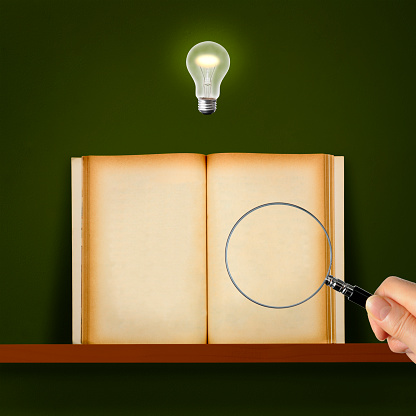 Close-up of blank old book on a shelf and a light bulb glowing in mid-air over the magnifying glass.