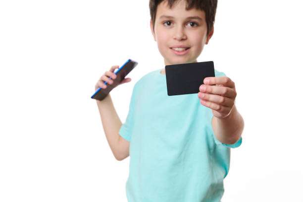白い背景にぼかした10代の少年の手にプロモーションテキスト用の空白スペースを持つ黒いクレジットカードに焦点を当てる - paying children only retail childhood ストックフォトと画像