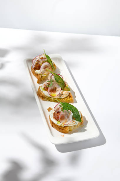 istock Aesthetic composition with tomato bruschetta on white background with harsh shadows. Italian bruschetta with tomatoes and cheese on fine dining in summer. Elegant menu concept. 1444342143