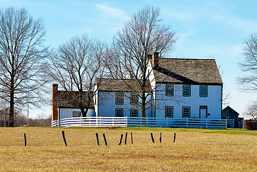 An old, rustic brick building stands in the middle of a wide and open field on a bright, sunny day