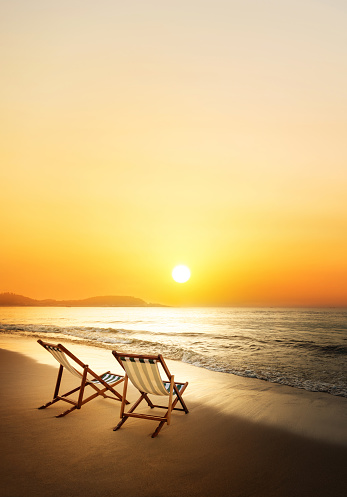 Two reclining chairs on the beach at sunrise