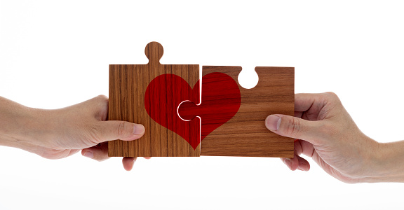 Two hands connecting or separating puzzle pieces with  red heart shape
