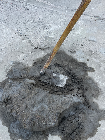 Stock photo showing close-up view of small pile of wet cement being spread over pavement with long handled concrete placer.