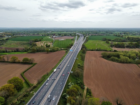 An aerial shot of a highway surrounded by green trees and a dry sandy land