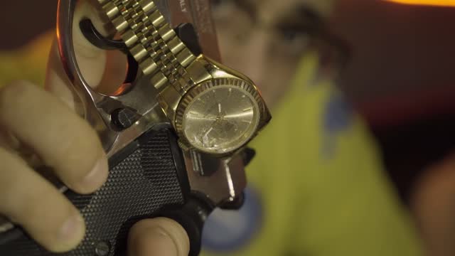 Closeup shot of a male hand holding a gun with a luxurious watch hanging on it in HD