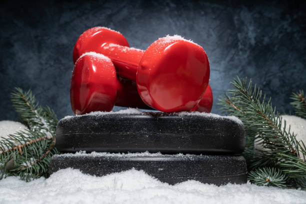 istock Winter composition with gym dumbbells on barbell weight plates and Christmas tree branches on a white snow. 1444372802