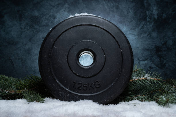 istock Winter composition for Christmas. Gym dumbbells barbell weight plate and tree branches on a white snow. 1444374639