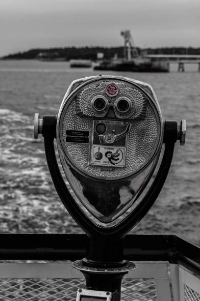 A vertical grayscale of a coin-operated binocular at a shore