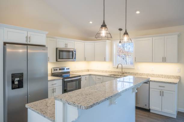 istock Cozy modern kitchen interior with white cupboards, fridge, oven, and lit lamps hanging on a ceiling 1444379911