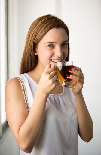 A woman holding glass of tea and looking at camera with smile in white background